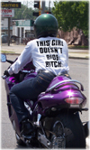 a photo of woman riding a motorcycle facing away from the viewer, on her shirt is the legend: THIS GIRL DOESN'T RIDE BITCH